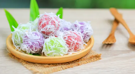 Klepon Ubi Ungu yang Lezat: Bola-bola klepon berbahan dasar ubi ungu, disajikan dengan lapisan kelapa parut yang lembut dan isian gula merah cair yang manis