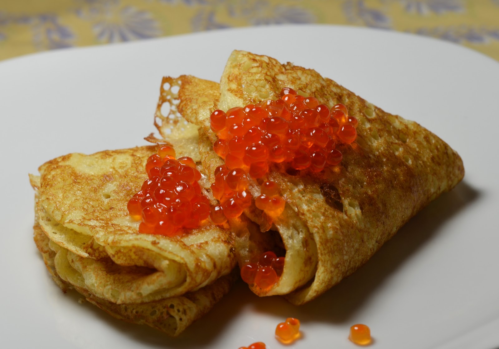 Plate of golden blini topped with sour cream and caviar
